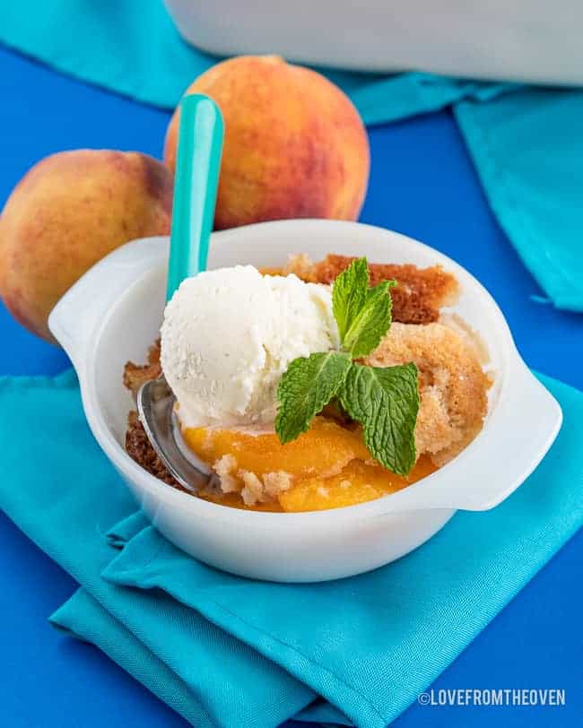 a bowl of peach cobbler made with canned peaches on a blue background