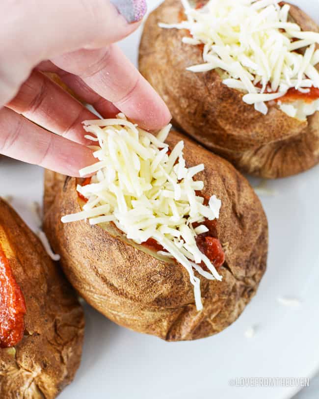 someone putting cheese on a baked potato