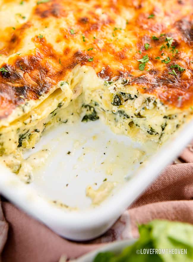 a casserole dish of alfredo lasagna with a slice taken out