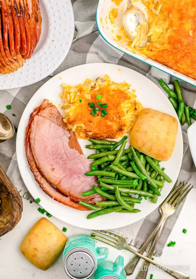 A plate full of food with green beans, ham and hashbrown casserole