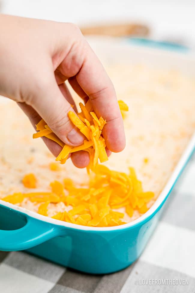 cheese being put on a potato casserole