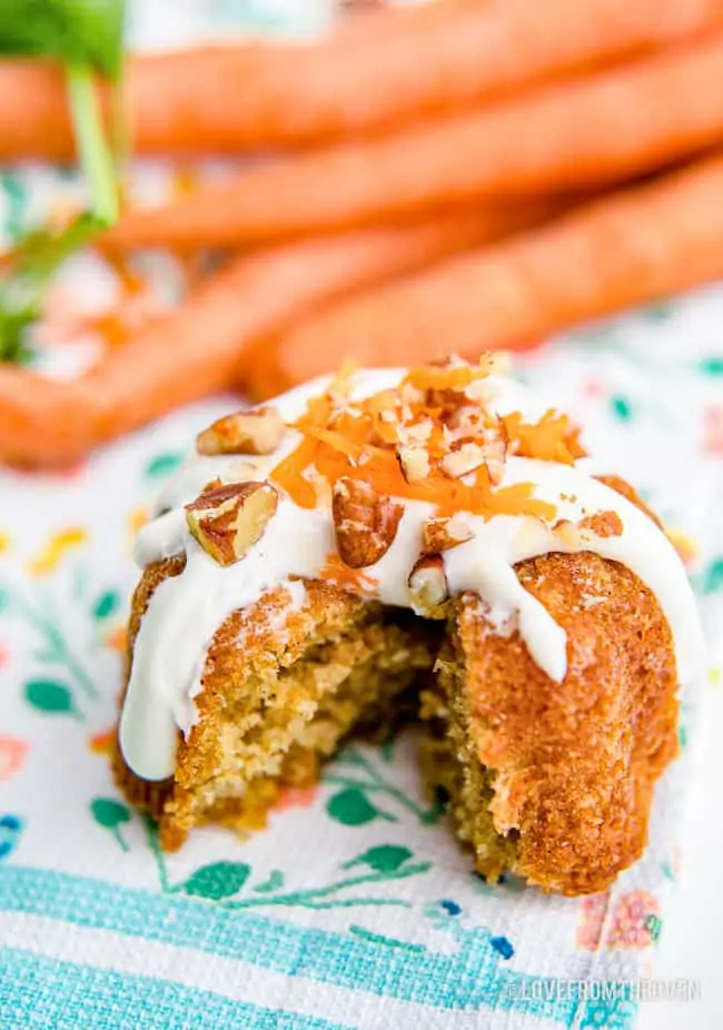 A mini carrot cake with a bite taken out and carrots