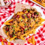 a basket of chili cheese fries on a red and white tablecloth