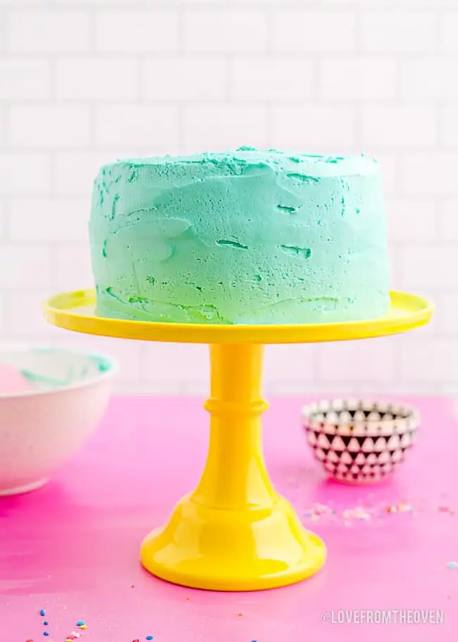 a blue frosted cake on a yellow cake stand