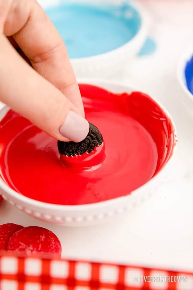 an oreo being dipped in red candy coating