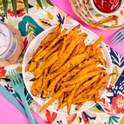 A plate of air fryer sweet potato fries on a pink background.