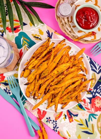 A plate of air fryer sweet potato fries on a pink background.
