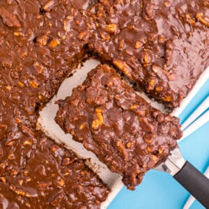 A slice of texas sheet cake being taken out of a sheet cake.