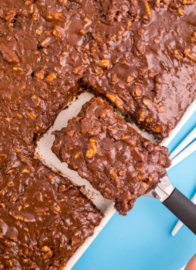 A slice of texas sheet cake being taken out of a sheet cake.