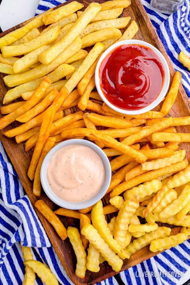 a variety of french fries on a platter with dipping sauces.