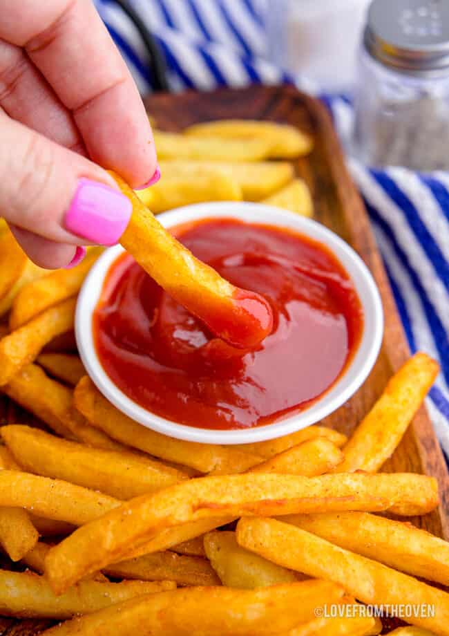 Someone dipping a fry into ketchup.