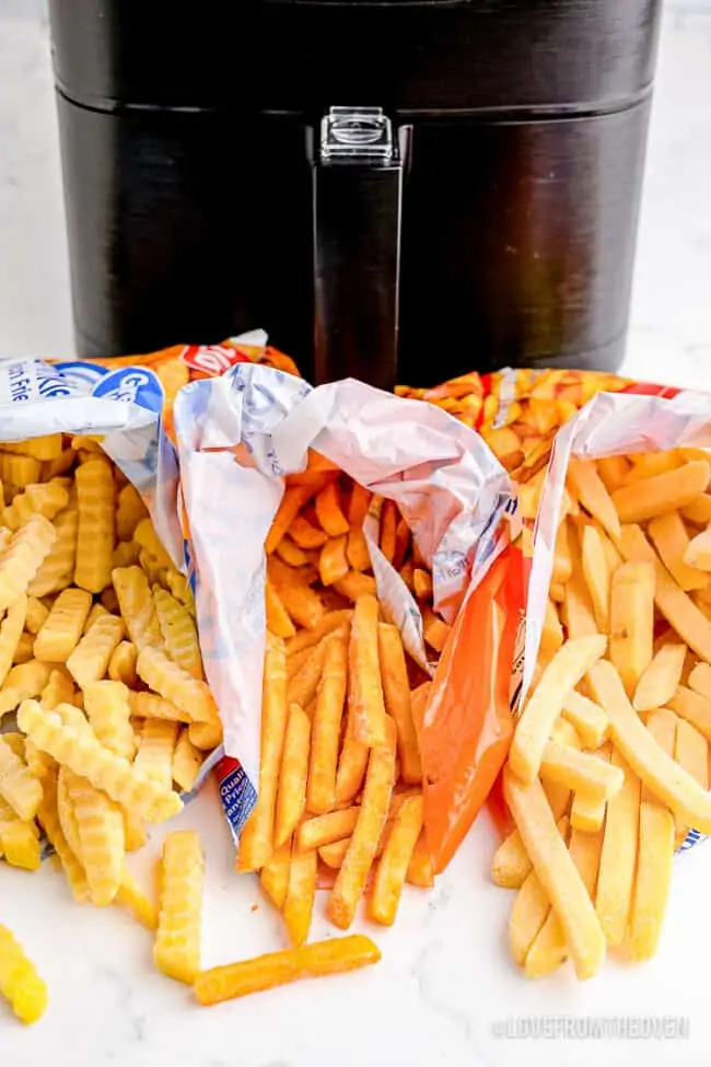 Bags of frozen french fries in front of an air fryer.