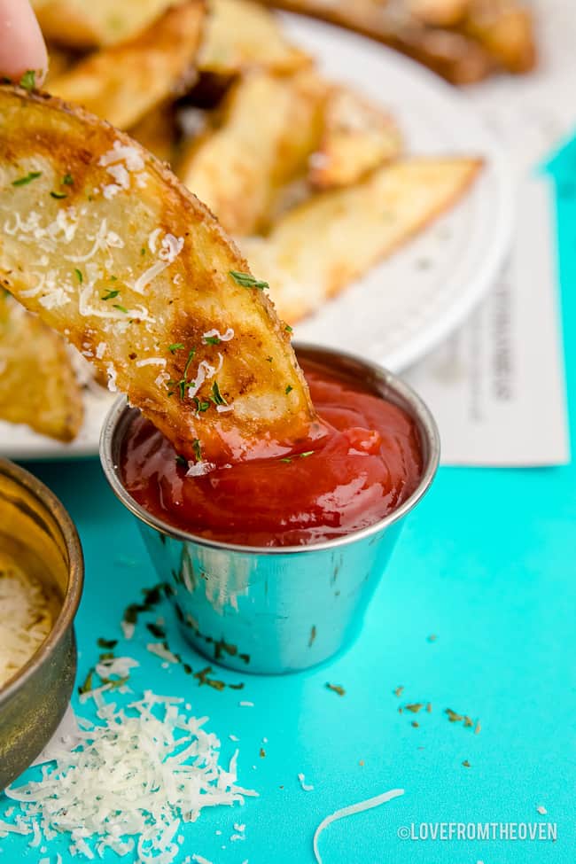 A potato wedge being dipped in ketchup.