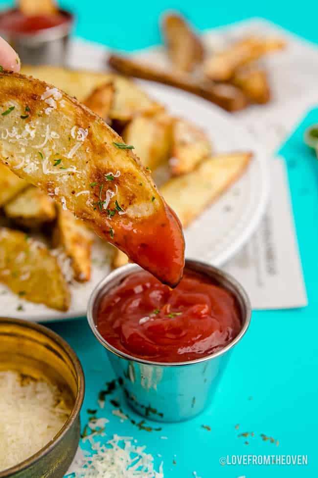 A potato wedge being dipped in ketchup.