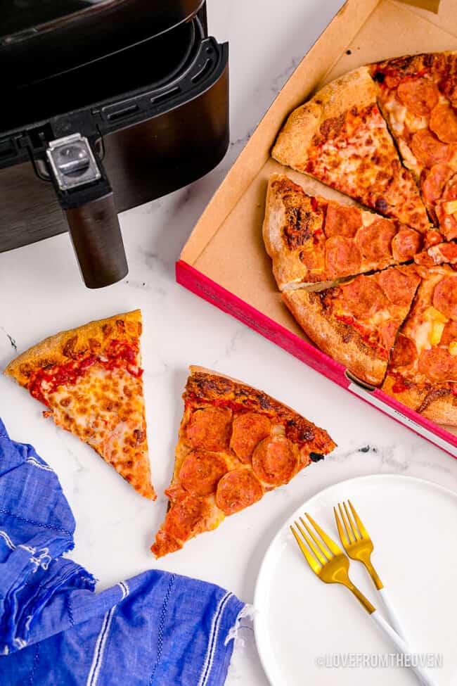 Cold pizza next to an air fryer.