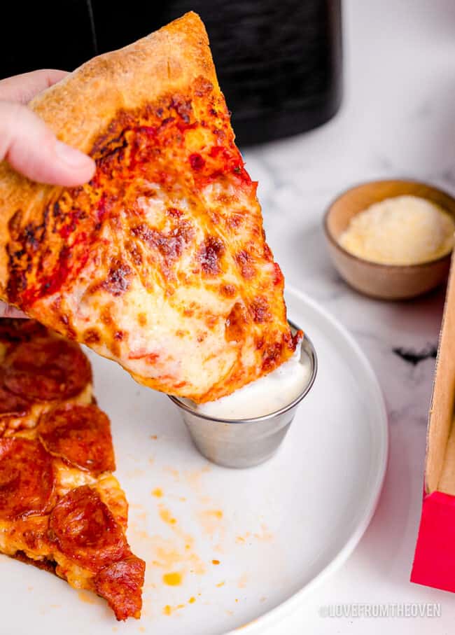 A slice of pizza being dipped in ranch dressling.