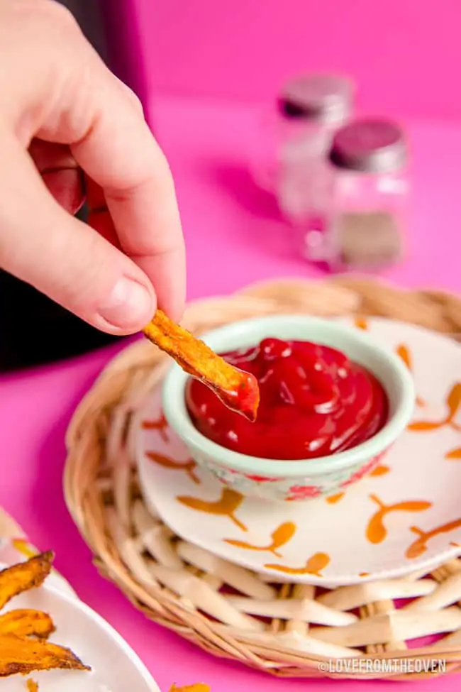 A sweet potato fry being dipped in ketchup.
