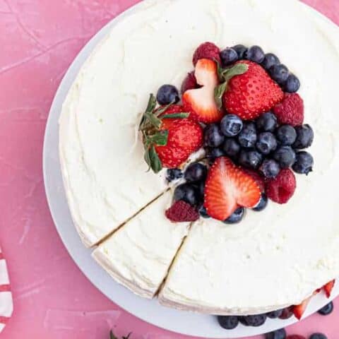 An overhead shot of a chantilly cake topped with berries on a pink background.