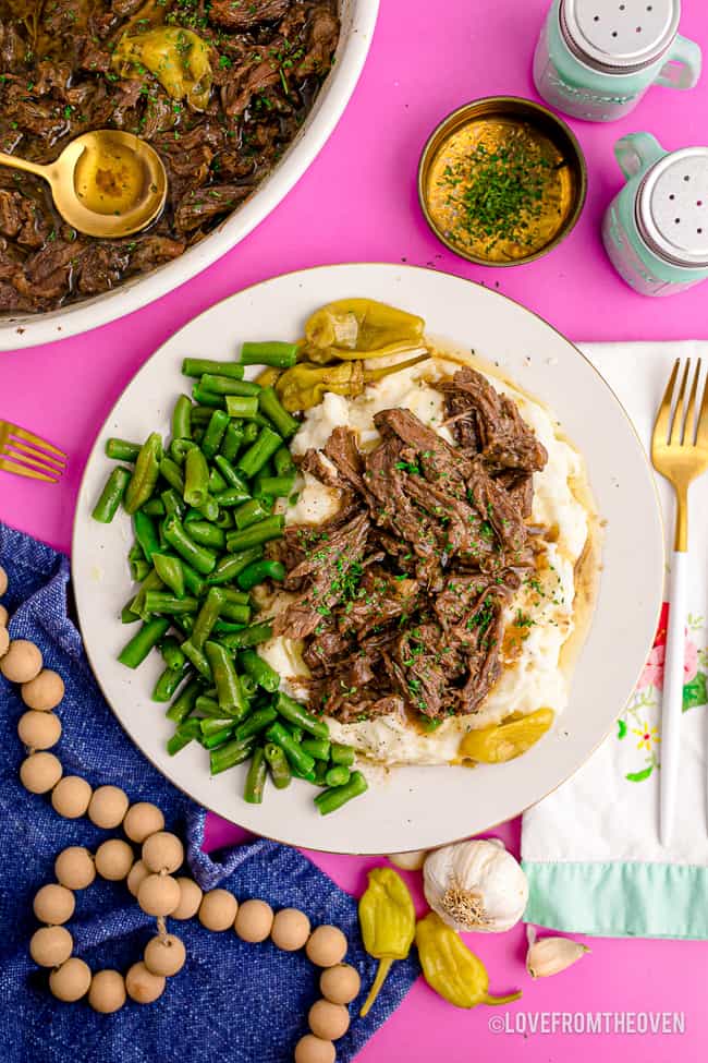 A plate of Mississippi pot roast with sides on a pink background