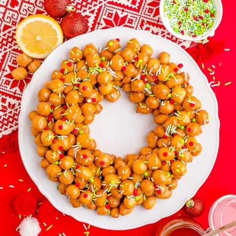 Struffoli on a white plate with a red background.