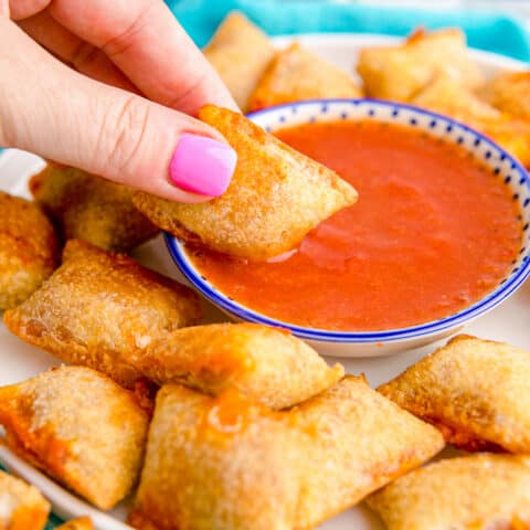 An air fryer pizza roll being dipped in tomato sauce.