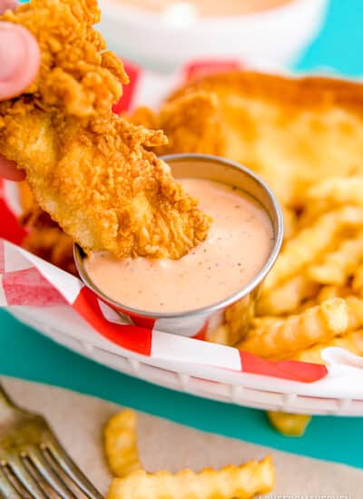 A piece of chicken being dipped into raising canes sauce.