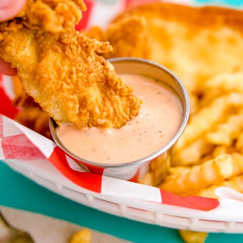 A piece of chicken being dipped into raising canes sauce.