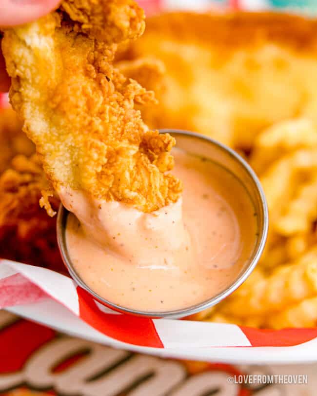 A piece of chicken being dipped in canes sauce.