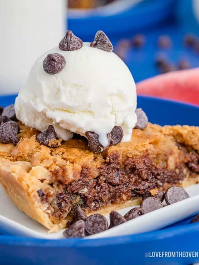 A close up photo of a piece of chocolate chip cookie pie topped with ice cream.