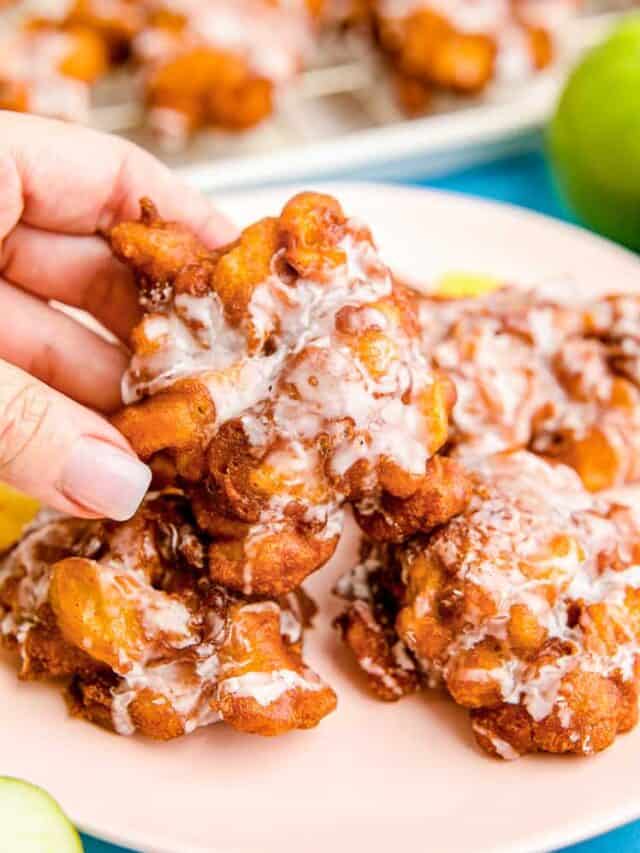 A hand grabbing an apple fritter from a plate.