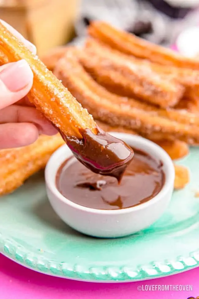 A churro being dipped in chocolate sauce.