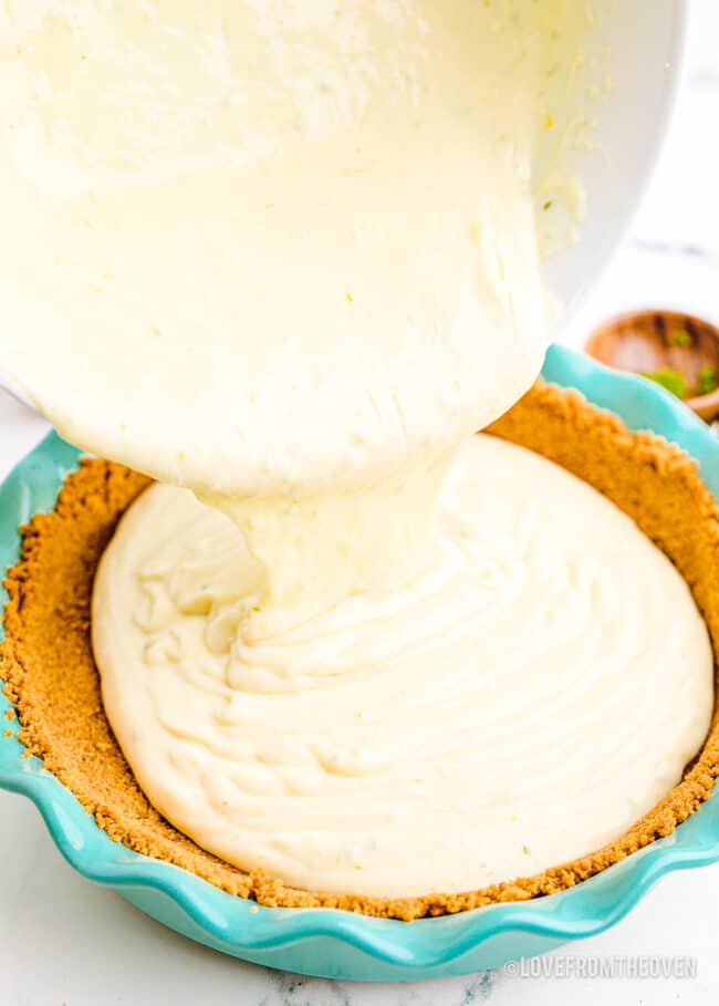 A pie filling being poured into a graham cracker crust.