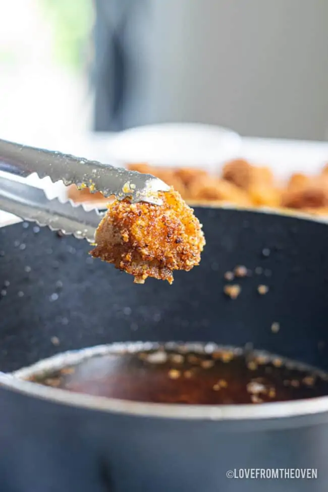 A piece of popcorn chicken over a pan of oil.