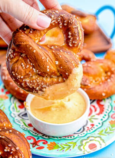 a homemade pretzel being dipped in cheese