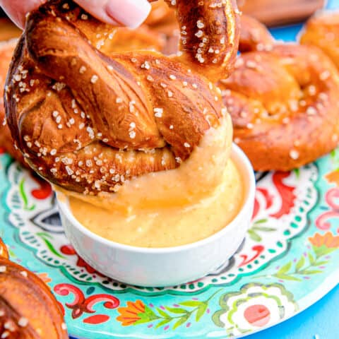 A homemade pretzel being dipped in cheese sauce