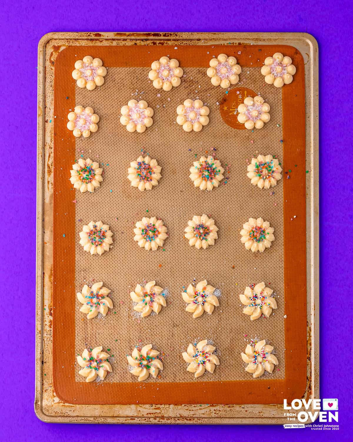 unbaked, pressed spritz cookies on a baking sheet topped with sprinkles