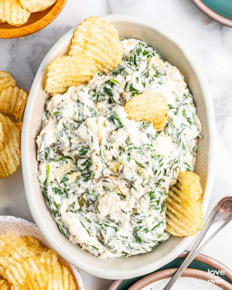 A white bowl of crockpot spinach artichoke dip.