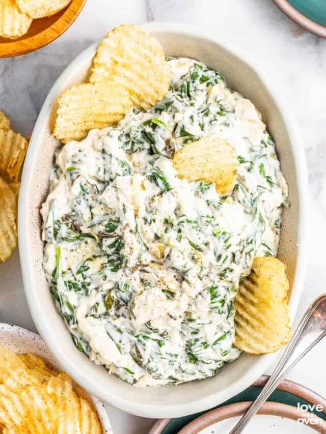A white bowl of crockpot spinach artichoke dip.