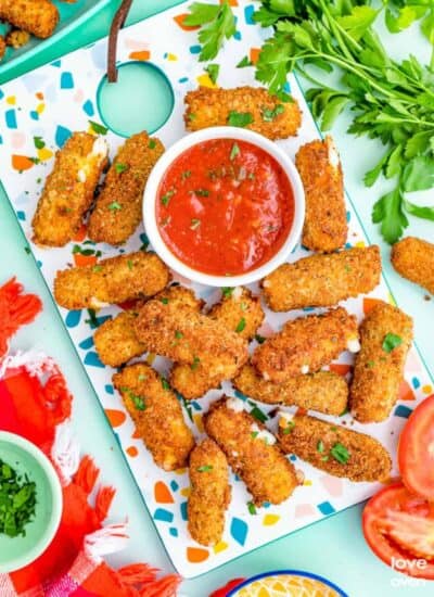 Mozzarella sticks and red sauce on a colorful background.