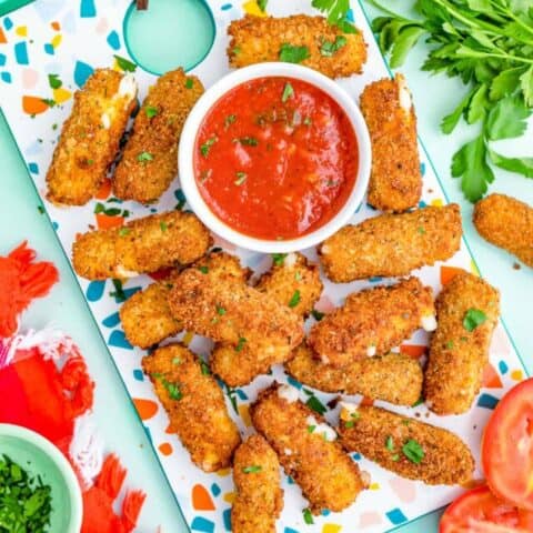 Mozzarella sticks and red sauce on a colorful background.