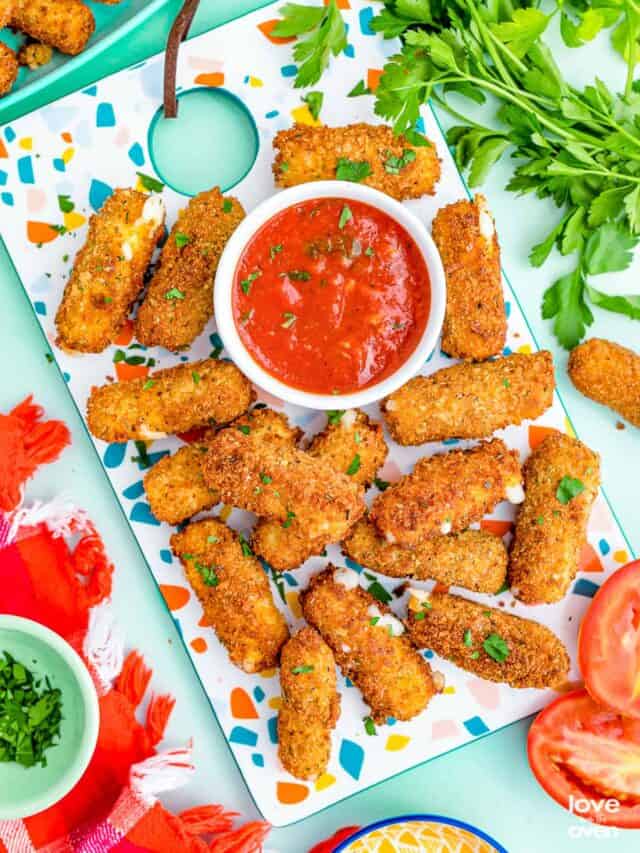 Mozzarella sticks and red sauce on a colorful background.