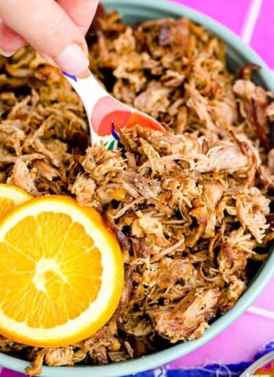 A close up of a pan of slow cooker pork carnitas with an orange and a spoon.