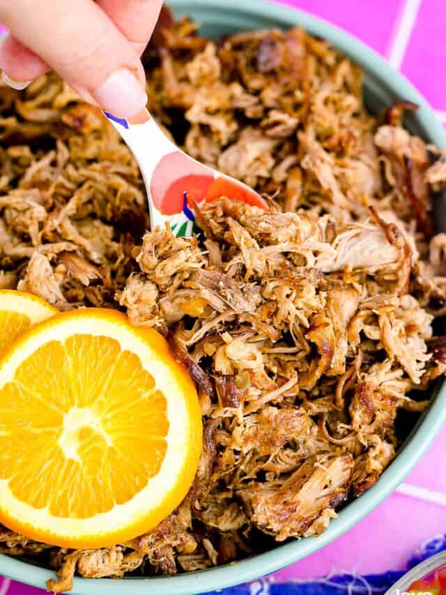 A close up of a pan of slow cooker pork carnitas with an orange and a spoon.