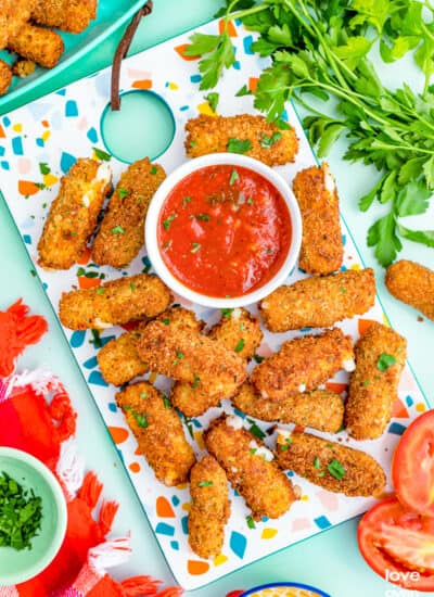 Mozzarella sticks and red sauce on a colorful background.