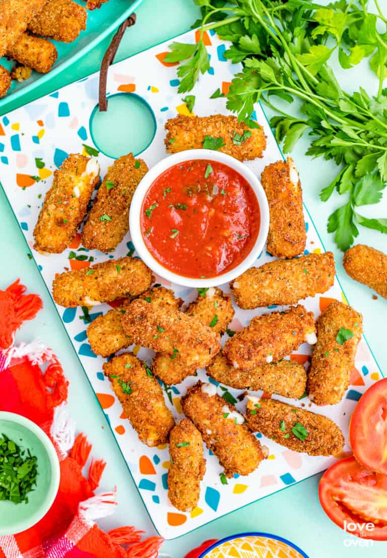 Mozzarella sticks and red sauce on a colorful background.