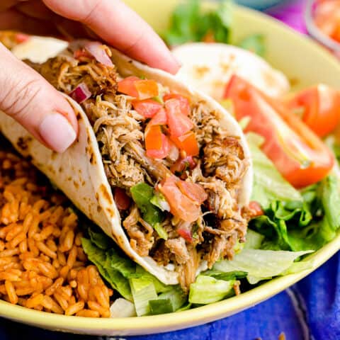 a hand picking up a pork carnita taco