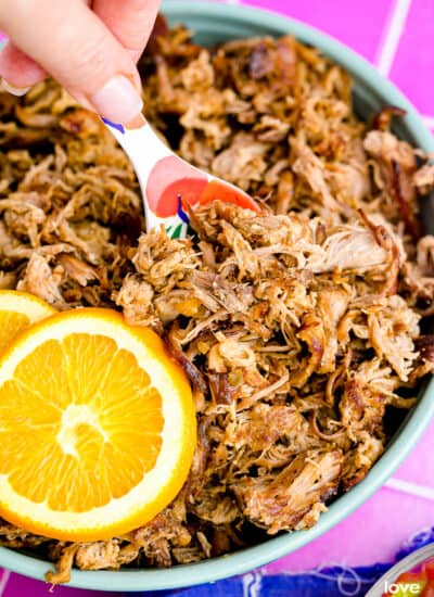 A close up of a pan of slow cooker pork carnitas with an orange and a spoon.