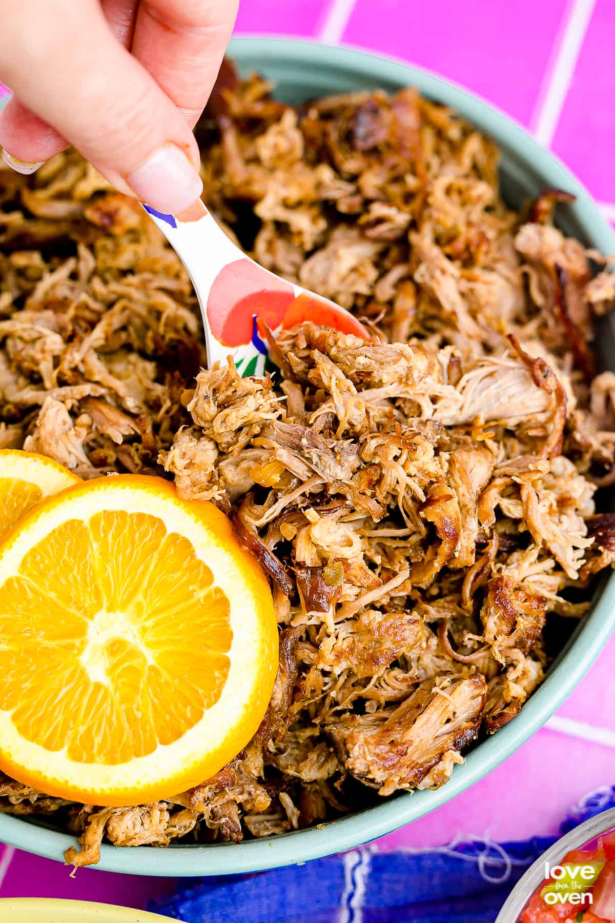 A close up of a pan of slow cooker pork carnitas with an orange and a spoon.