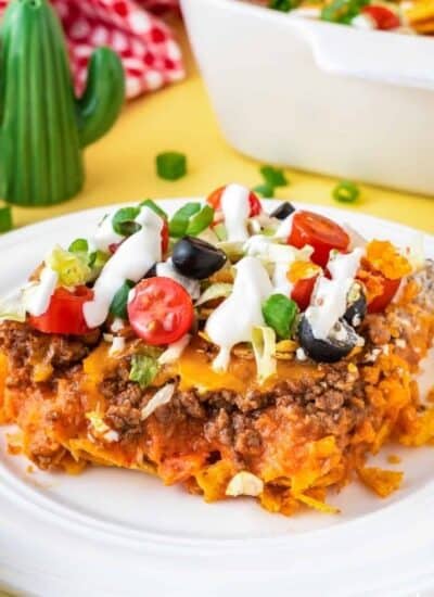 A taco casserole topped with fresh tomatoes, olives, spring onions and dressing