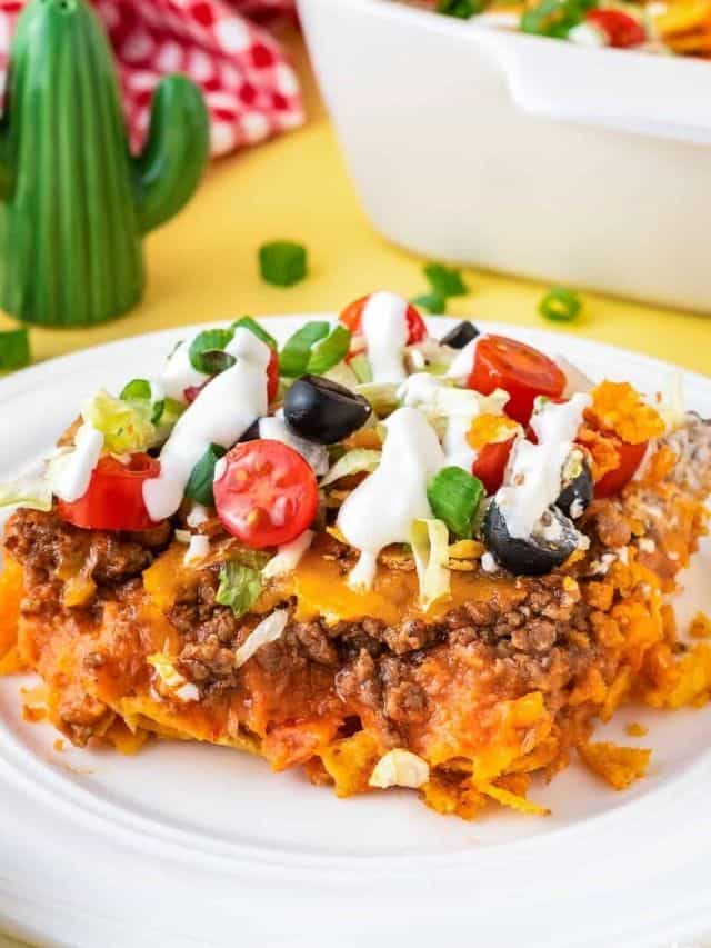 A taco casserole topped with fresh tomatoes, olives, spring onions and dressing